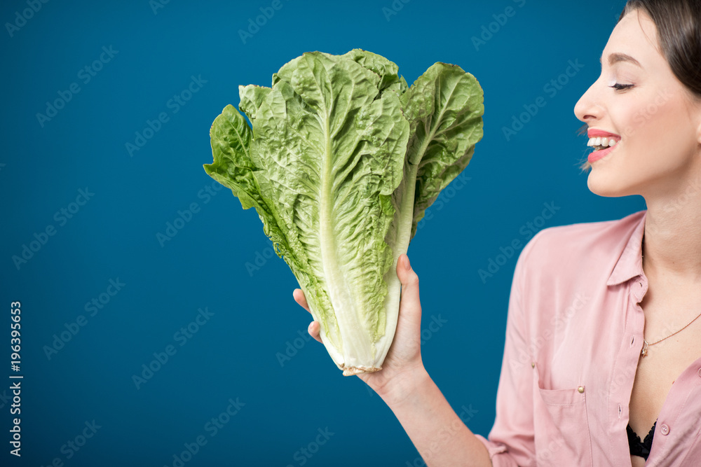 Woman holding a green lettuce on the blue wall background