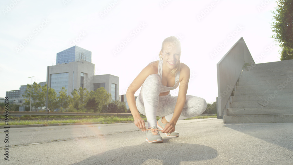 肖像：快乐的金发女孩系着灰色运动鞋的鞋带。