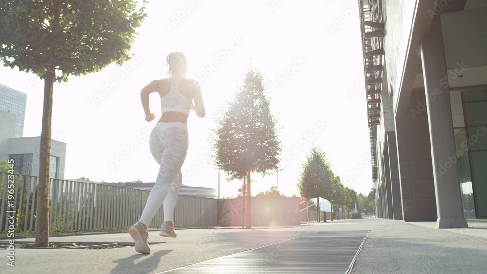 LOW ANGLE, LENS FLARE: Active woman exercising alone in pleasant morning sun.