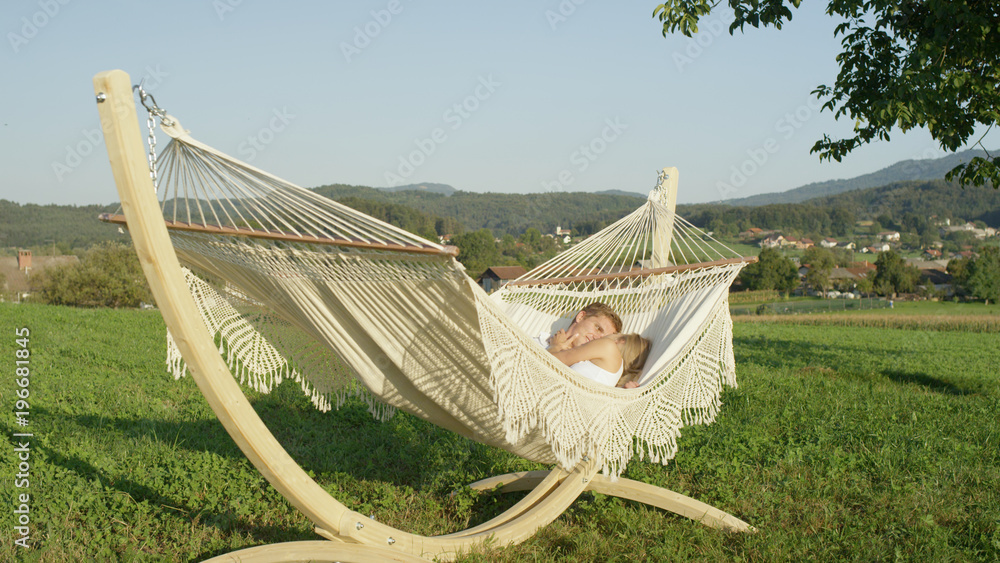 Lovestruck couple talks and cuddles on fabric sling during lovely date outdoors.