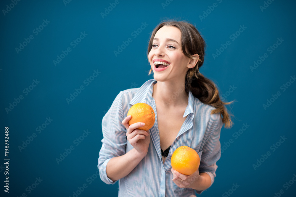 Portrait of a young and happy woman with oranges on the blue wall background