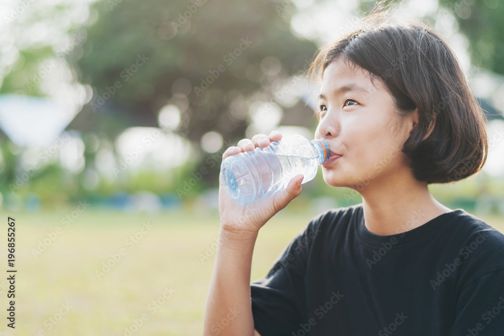 亚洲小女孩用日落背景的塑料瓶喝淡水