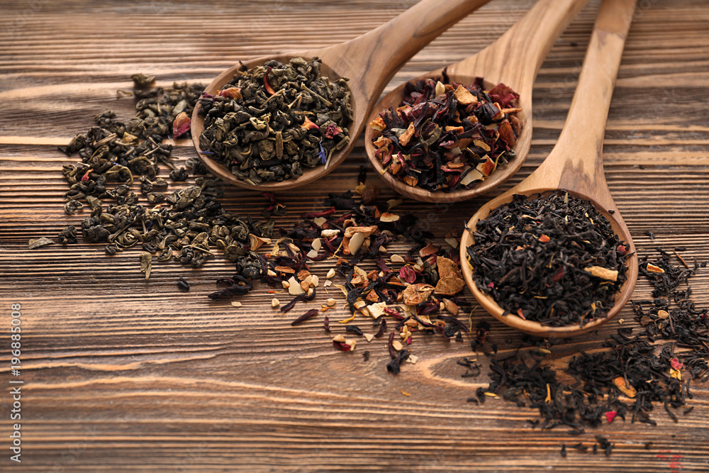 Spoons with different types of dry tea leaves on wooden background