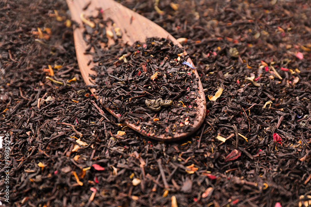 Dry black tea leaves with flower petals and spoon on table