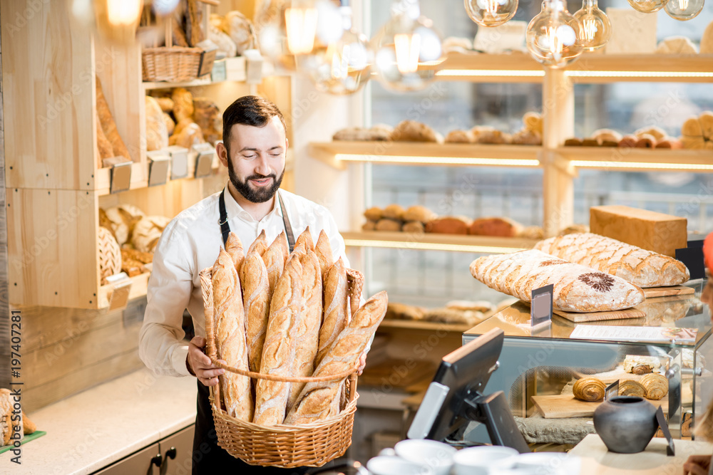 Handsome bread seller with basket full of baguettes in the beautiful store with bakery products