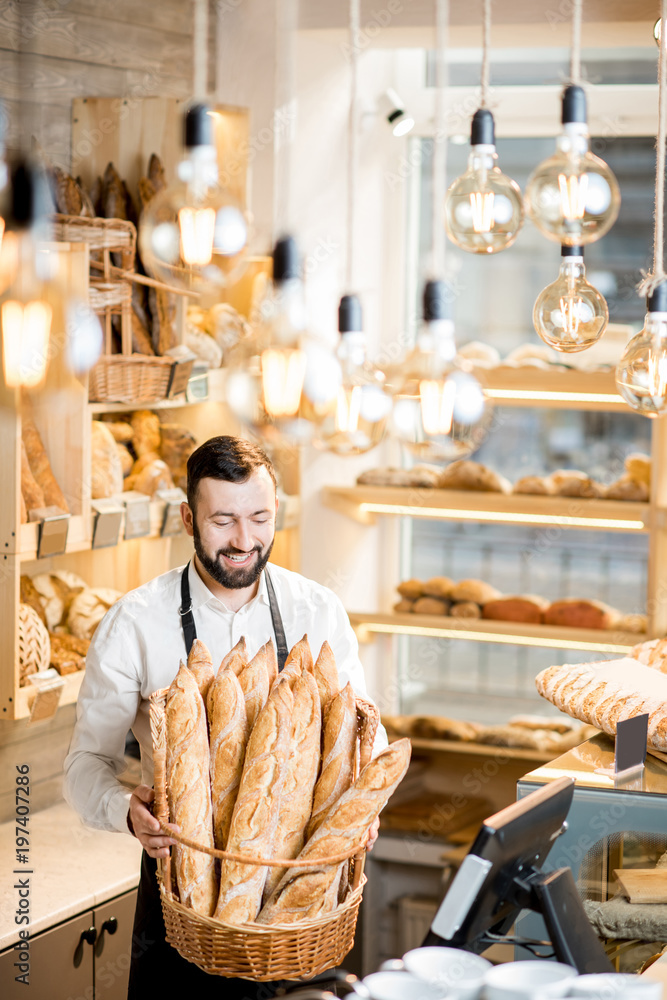 Handsome bread seller with basket full of baguettes in the beautiful store with bakery products