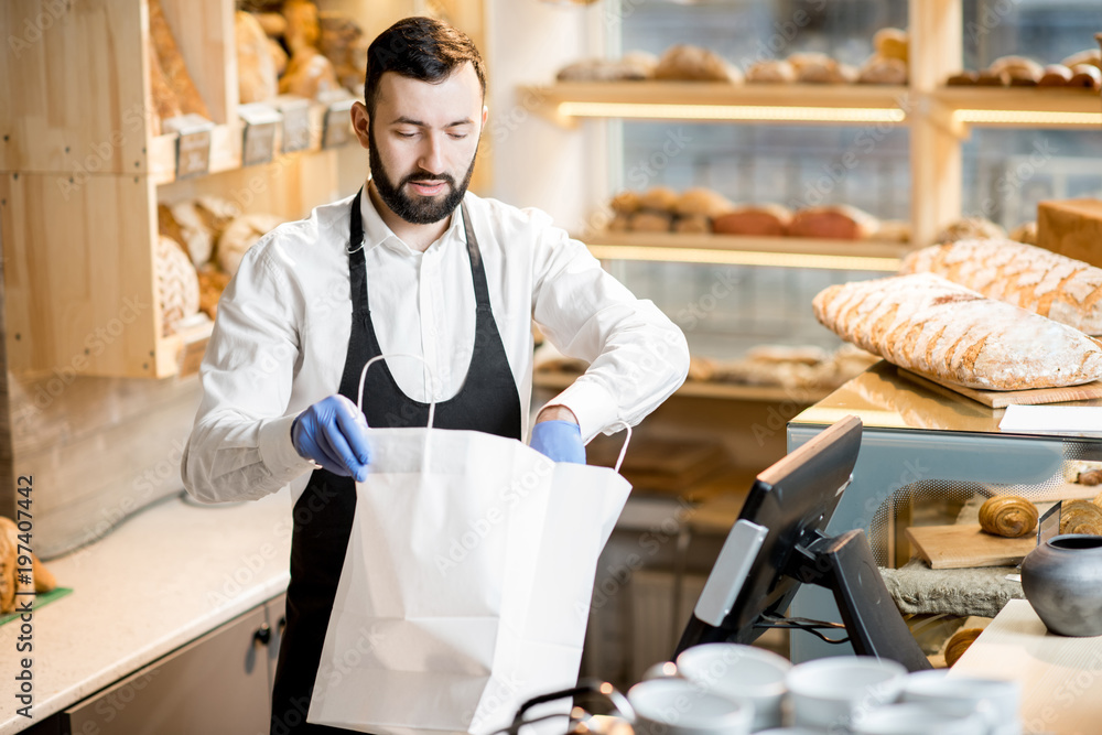 Bread seller packing a baguette into the paper bag in the store with bakery products