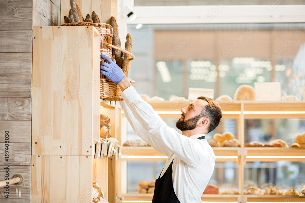 Seller putting a basket full of baguettes in the store with bakery products