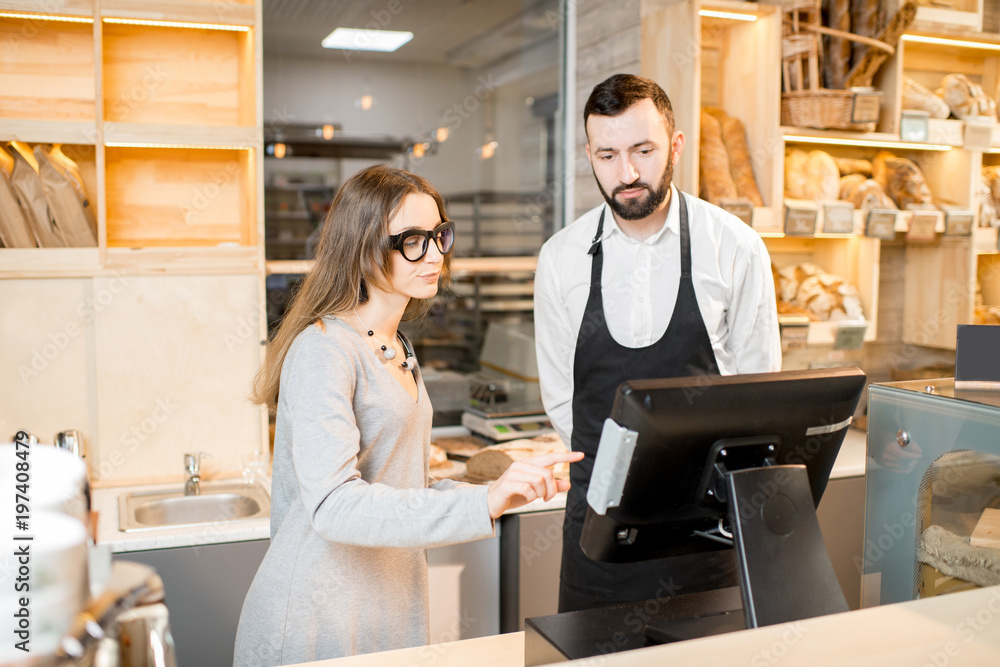 Young female owner of the bakery store with bread seller talking together in the shop