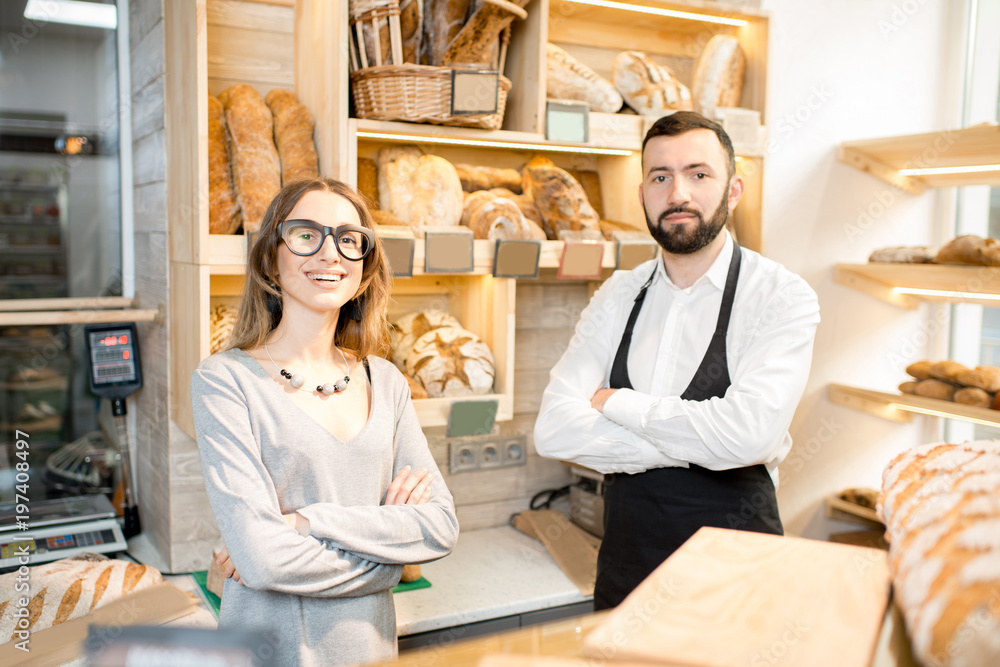 Young female owner of the bakery store with bread seller talking together in the shop