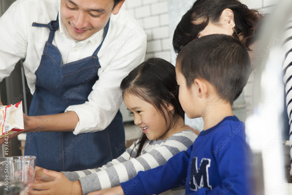 女の子が計量カップを持っている。お父さんが小麦を入れるところ。料理の手伝い。