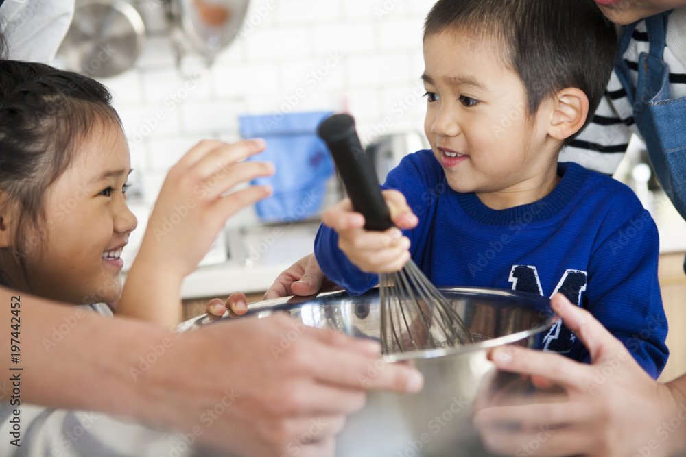 男の子がボウルに入ったピザ生地をかき回している。笑顔の男の子と女の子。お手伝い。