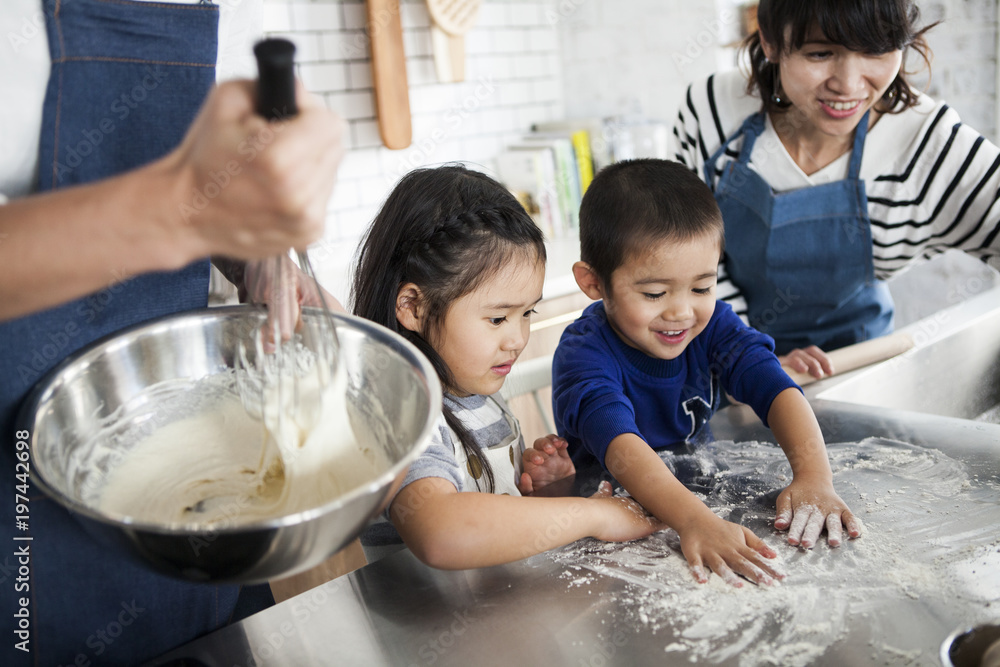 男の子と女の子がキッチンで料理の手伝いをしている。小麦粉をしいて、ピザ生地をこねることろ。