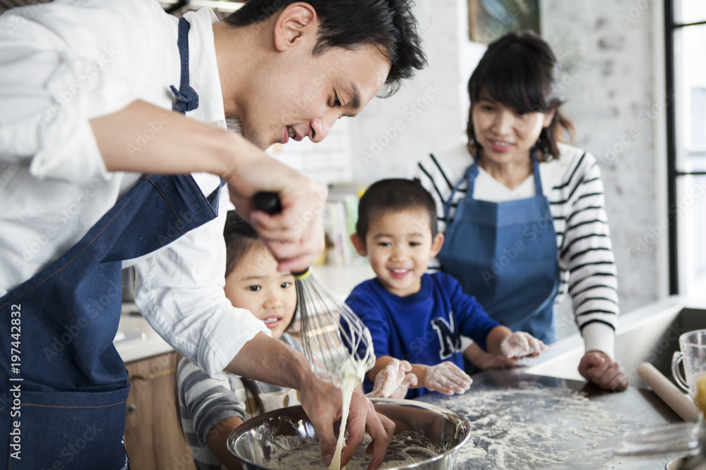 お父さんがピザの生地を作っている。楽しそうに見ているお母さんと娘と息子。