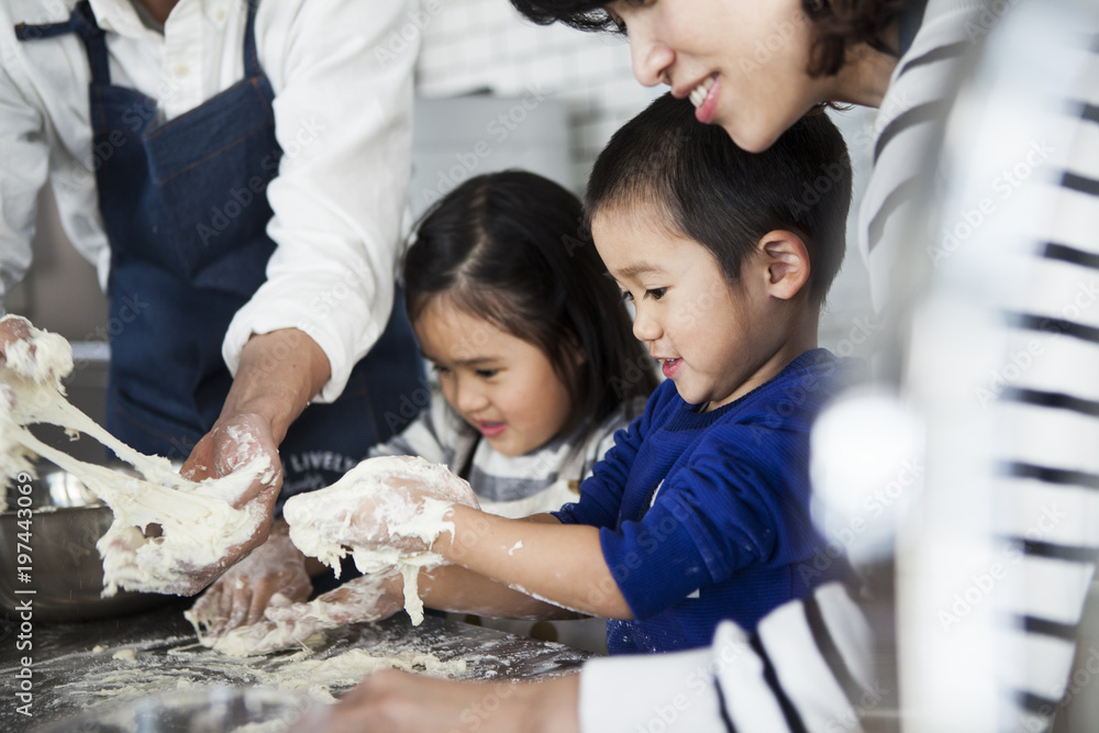 家族四人で仲良く料理を作っている。男の子と女の子はピザ生地をこねている。