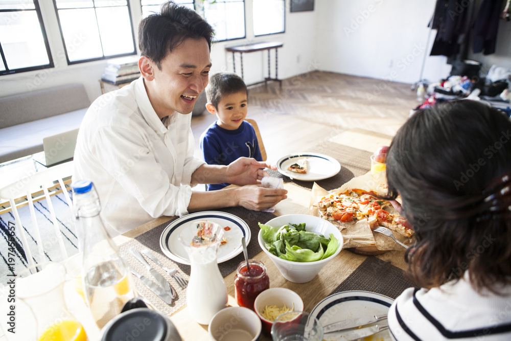 お父さんと息子がピザを食べている。笑顔。