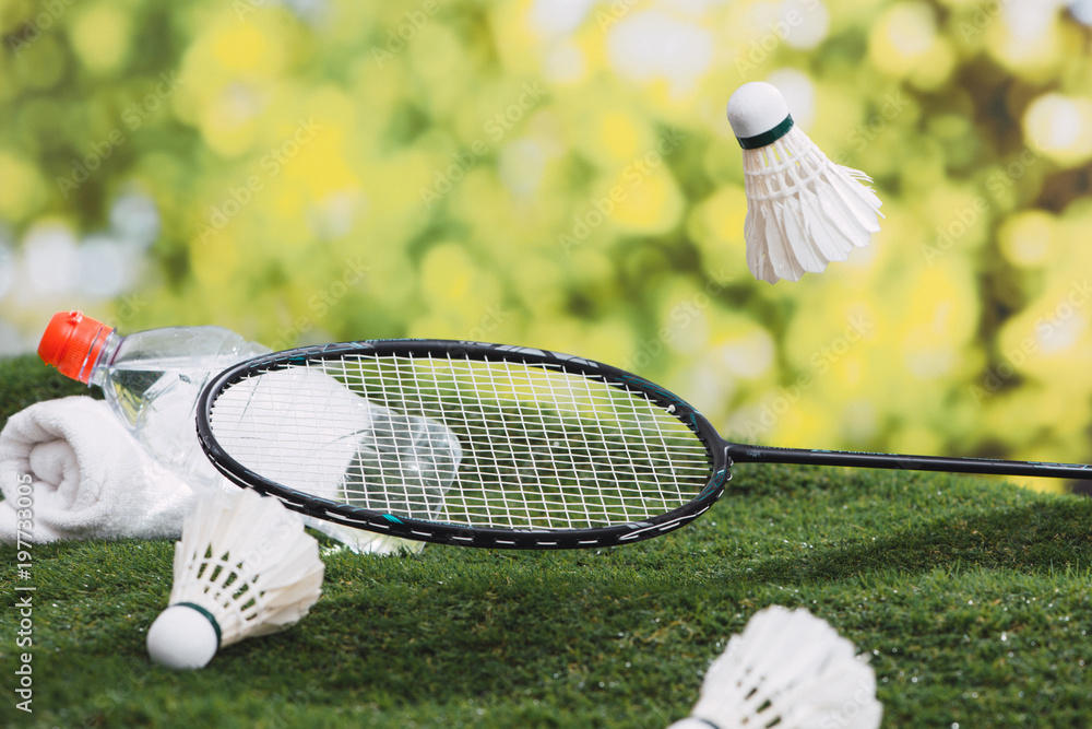 Shuttlecock and badminton racket with water and towel on the grass in the park.