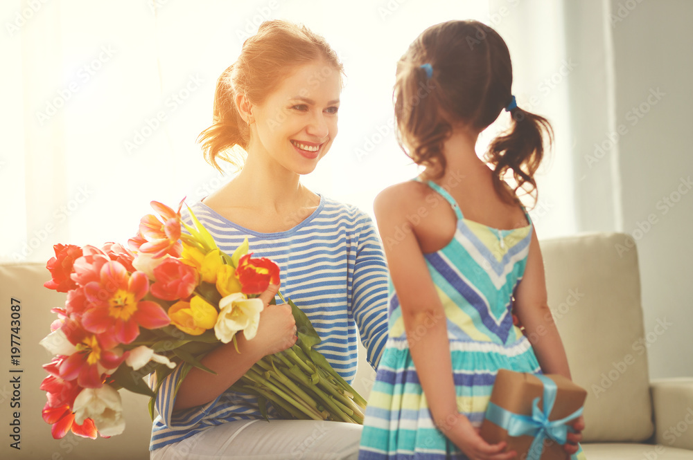 happy mothers day! child daughter   gives mother a bouquet of flowers to tulips and gift