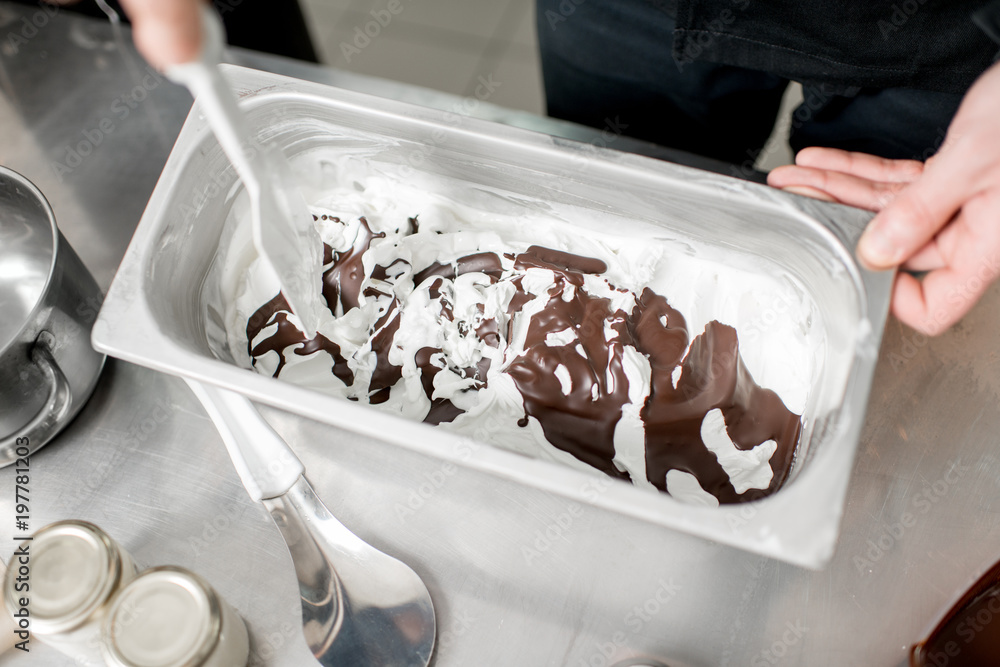 Chef mixing ice cream with chocolate in the metal tray on the kitchen