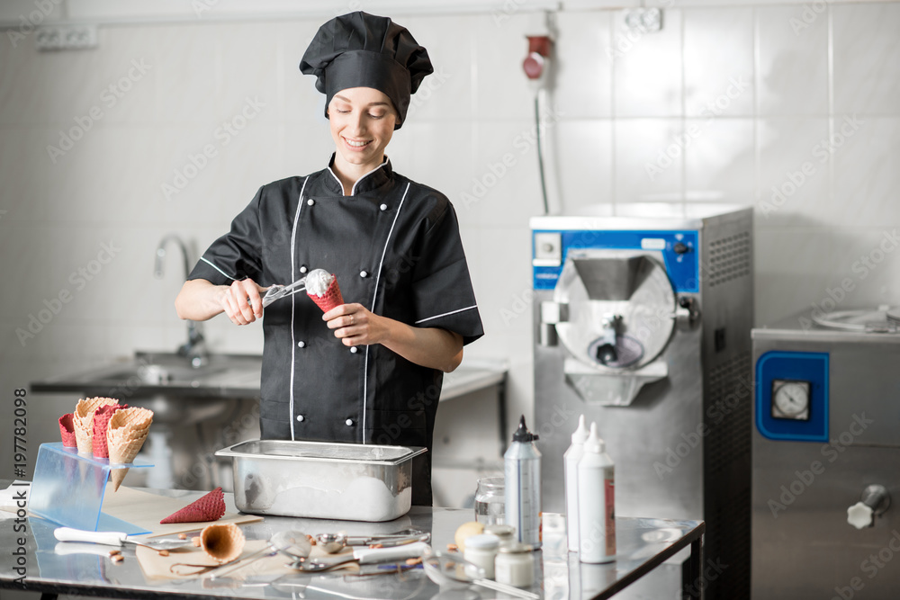 Young female chef cook filling with ice cream a waffle cone standing in the professional kitchen