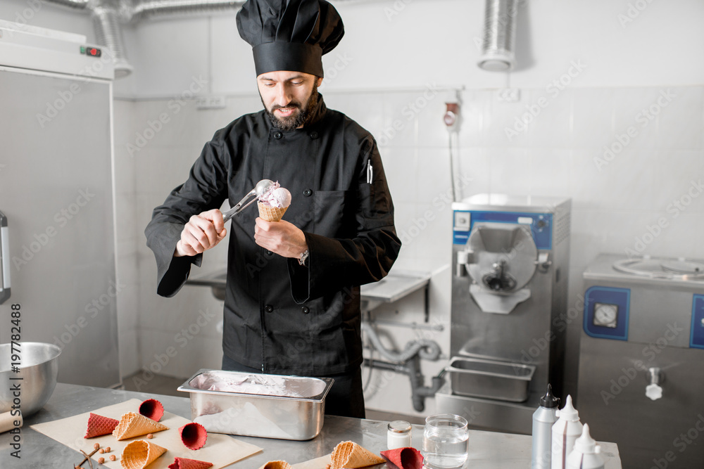 Chef cook in uniform filling with ice cream a waffle cone standing in the professional kitchen