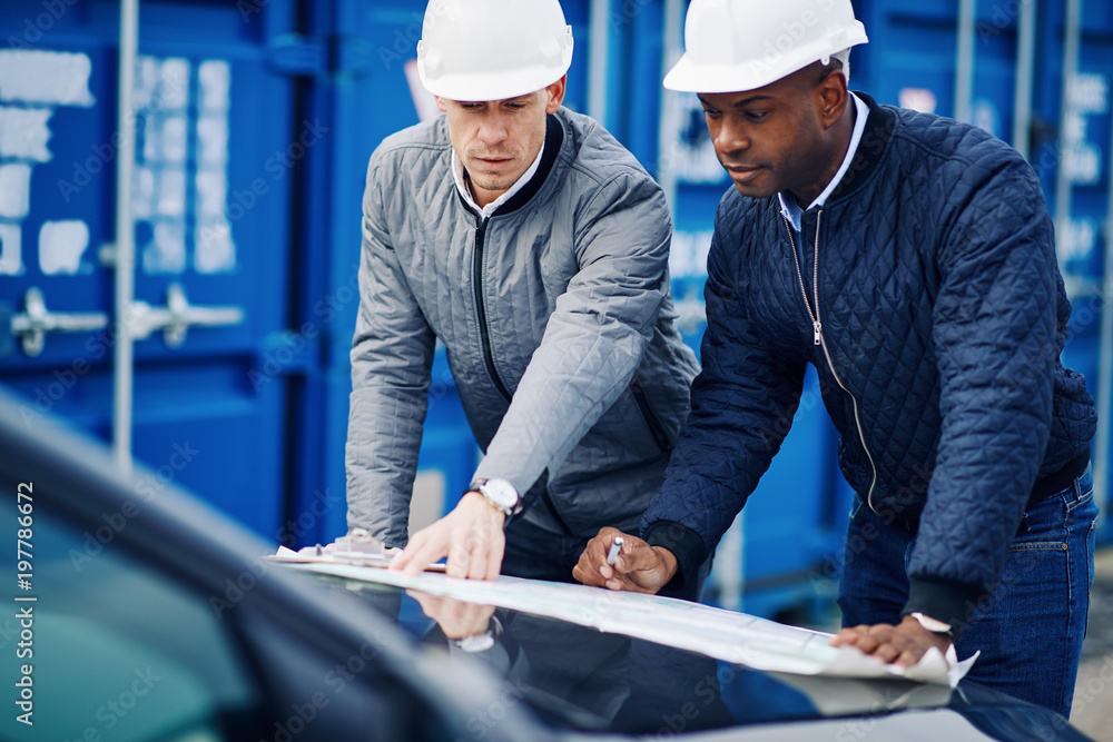 Freight engineers leaning on a truck discussing blueprints