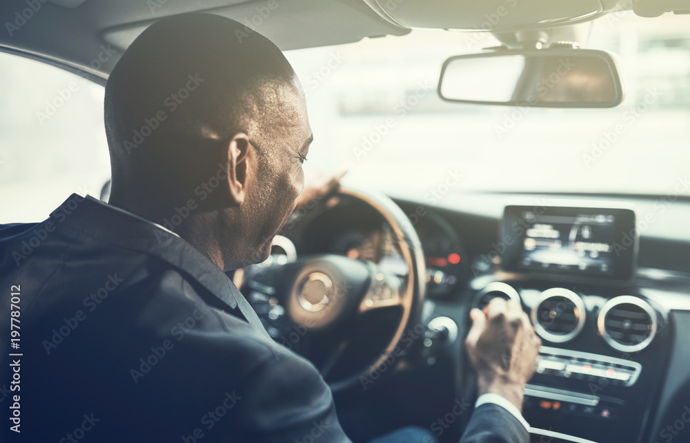 Young African businessman listening to music while driving to wo