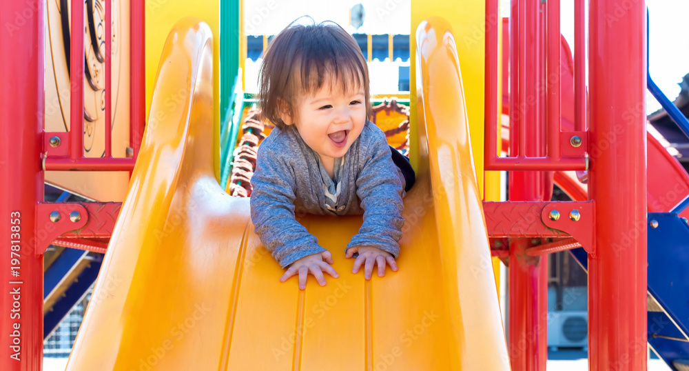 Mixed race toddler boy playing on a slide at a playground