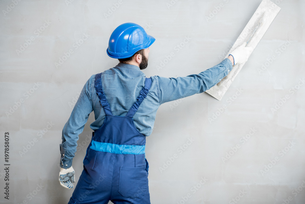 Plasterer in blue working uniform plastering the wall indoors