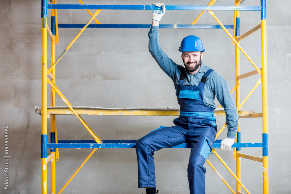 穿着蓝色工作服的建筑工人坐在室内脚手架上