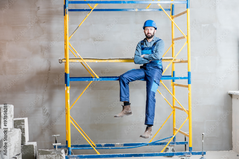 穿着蓝色工作服的建筑工人坐在室内脚手架上