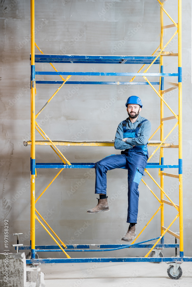 穿着蓝色工作服的建筑工人坐在室内脚手架上