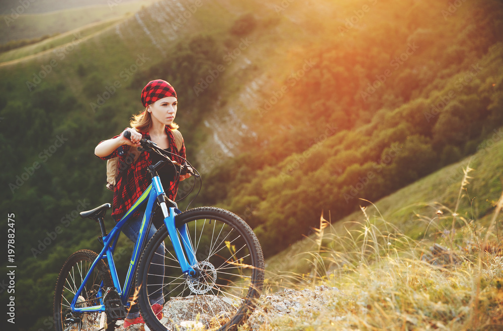 Woman tourist on a bicycle at top of mountain at sunset outdoors during a hike in summer