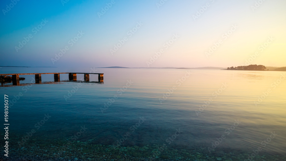 暖色的平静海景。夏天日落时的码头和大海。夜晚放松的海洋背景