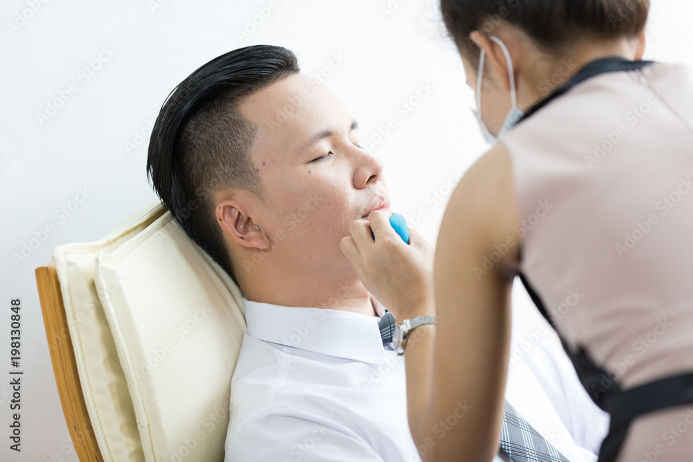 Professional Make-up artist doing young asian man makeup in office.