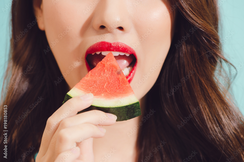 Attractive young asian woman eating slice of watermelon, closeup.