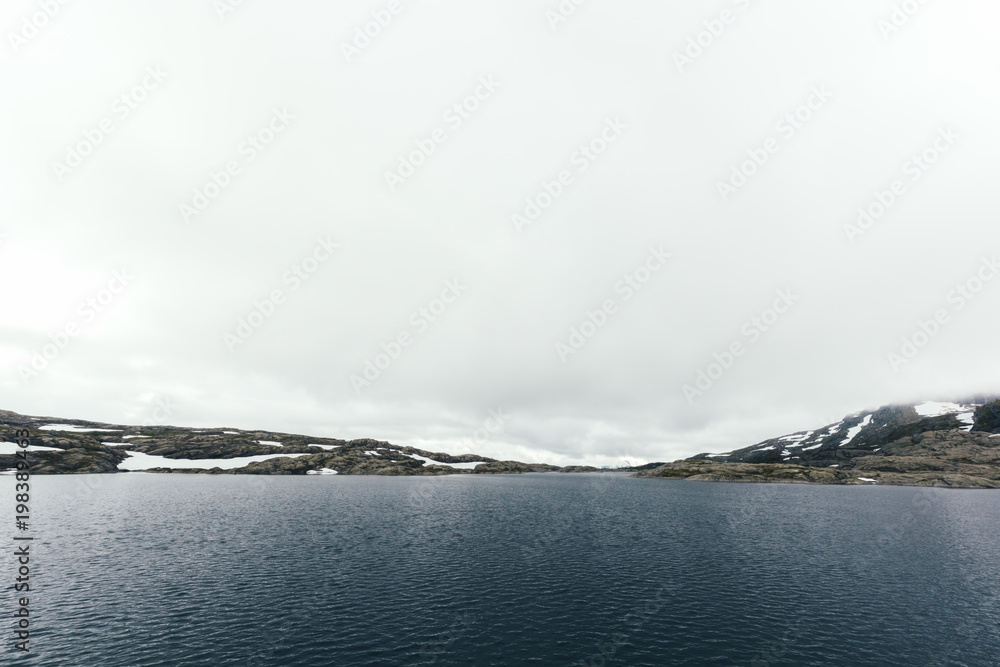 Typical norwegian landscape with snowy mountains and clear lake near the famous Trolltunga rock, Nor