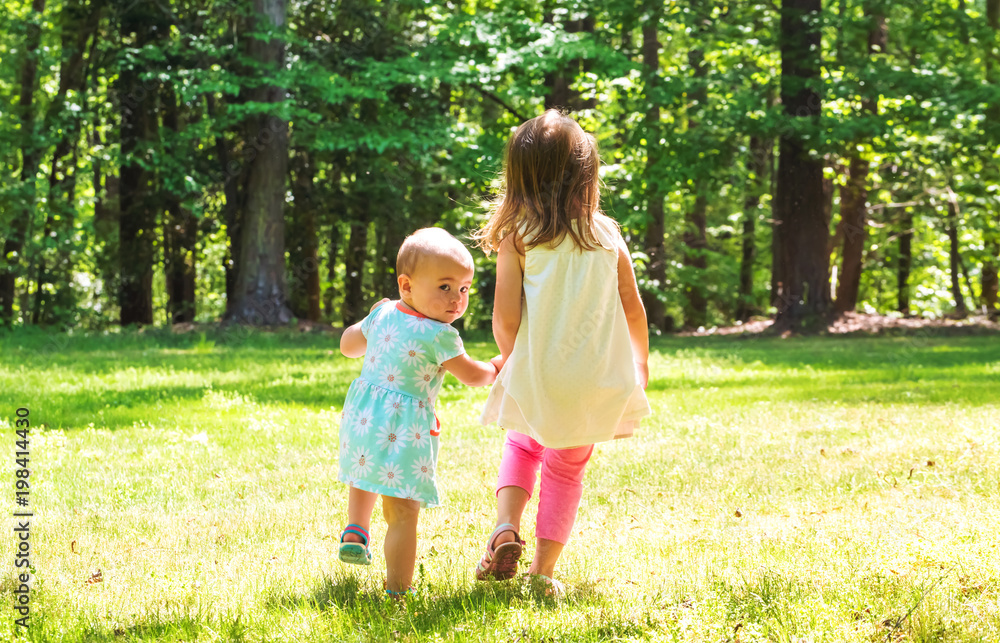 Two young sisters holding hands outside on a warm day