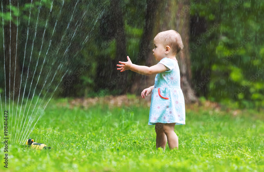 Happy toddler girl playing in a water sprinkler outside