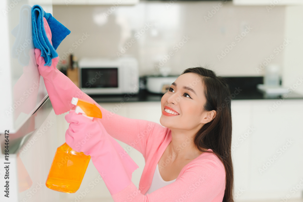 Beautiful asian woman in protective gloves cleaning kitchen cabinet