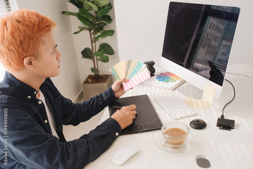 Smiling photo editor working on computer at desk with camera and graphics tablet