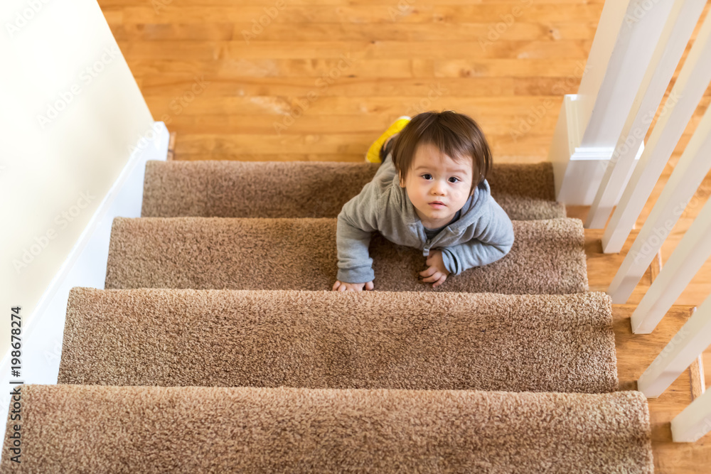 Toddler boy climbing a staircase in his house