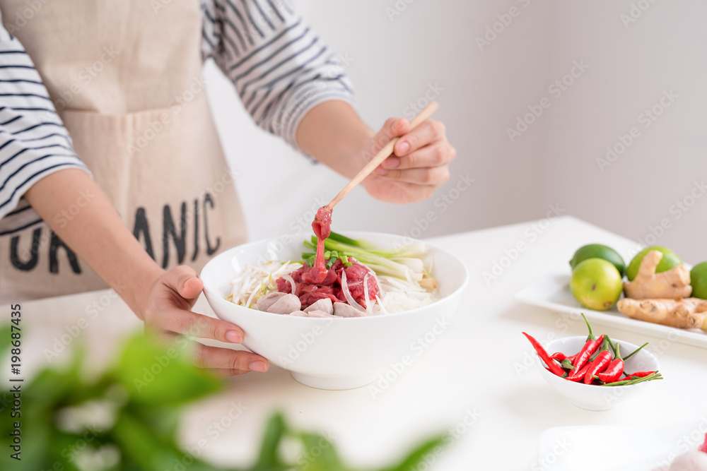 Female chef prepare traditional Vietnamese soup Pho bo with herbs, meat, rice noodles