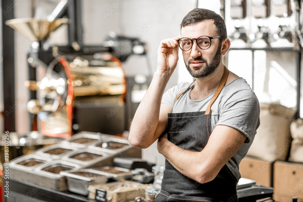 Portrait of a handome bearded barista in uniform standing in the coffee shop with coffee roaster mac