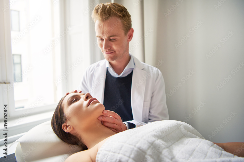 Cosmetologist holding and looking on young woman face