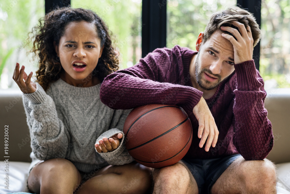 Young couple watching basketball match at home