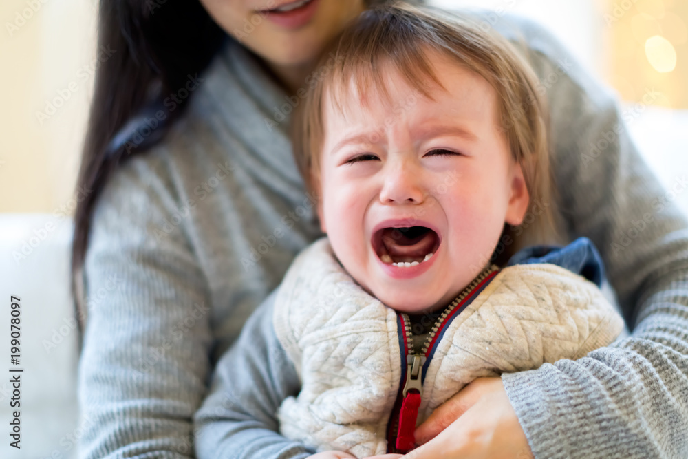 Upset toddler boy crying in his mothers arms