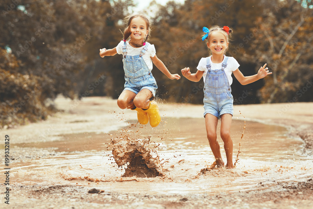 Happy funny sisters twins child girl   jumping on puddles in rubber boots  .