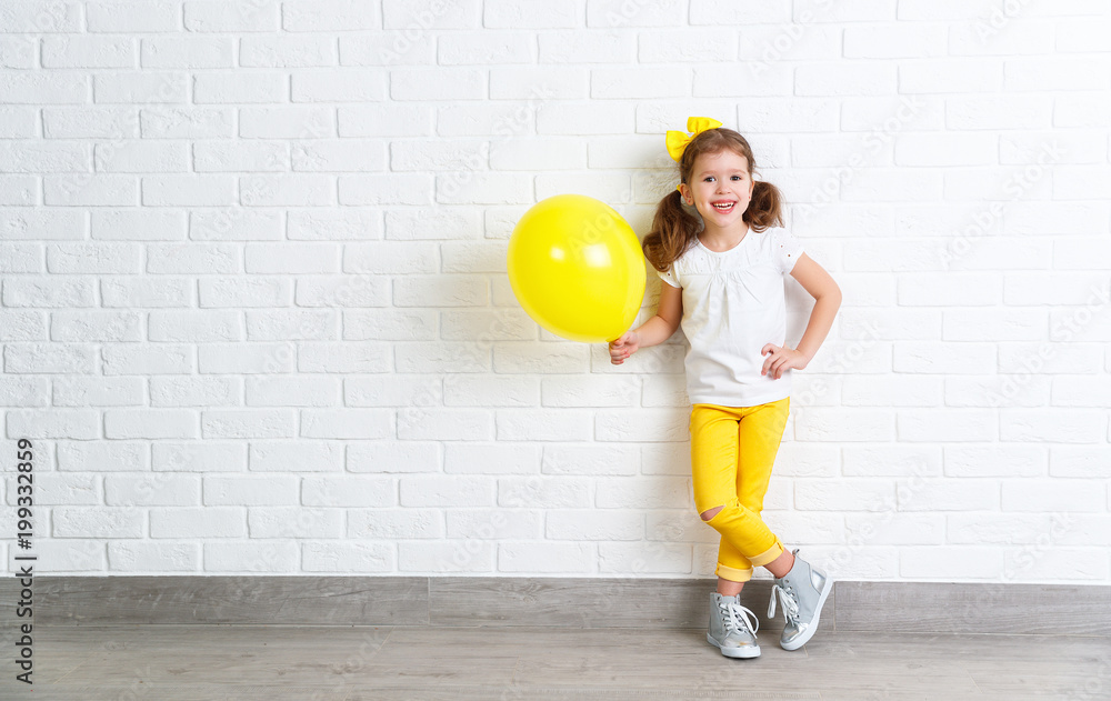 happy funny child girl with yellow   balloon near an empty wall.