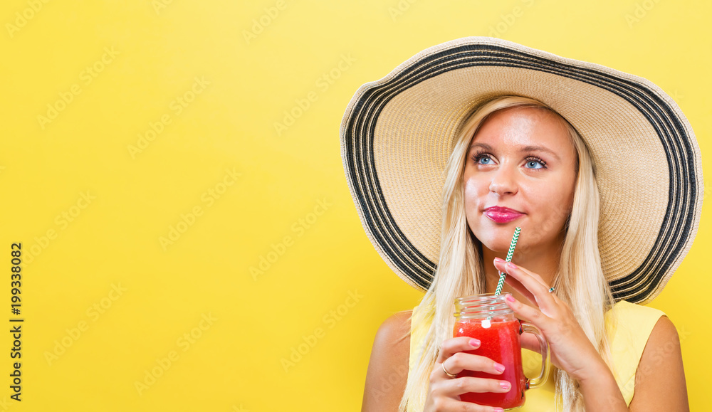 Happy young woman drinking smoothie on a yellow background